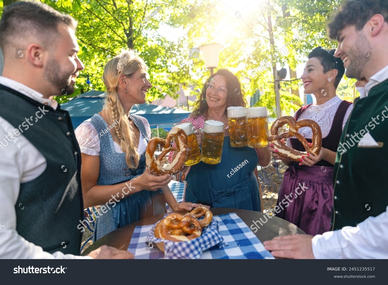 Waitress serving beer to a group of happy friends in traditional tracht at oktoberfest or beer garden in germany #2451235517
