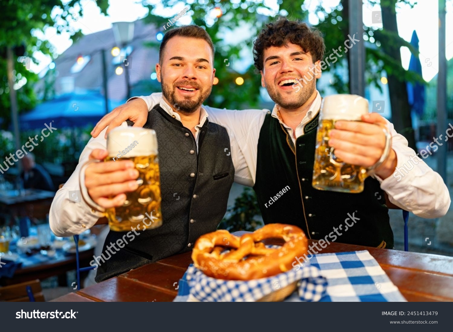 In Beer garden or Oktoberfest - Happy friends in Tracht, Dirndl and Lederhosen drinking fresh beer in mugs at Bavaria, Germany #2451413479