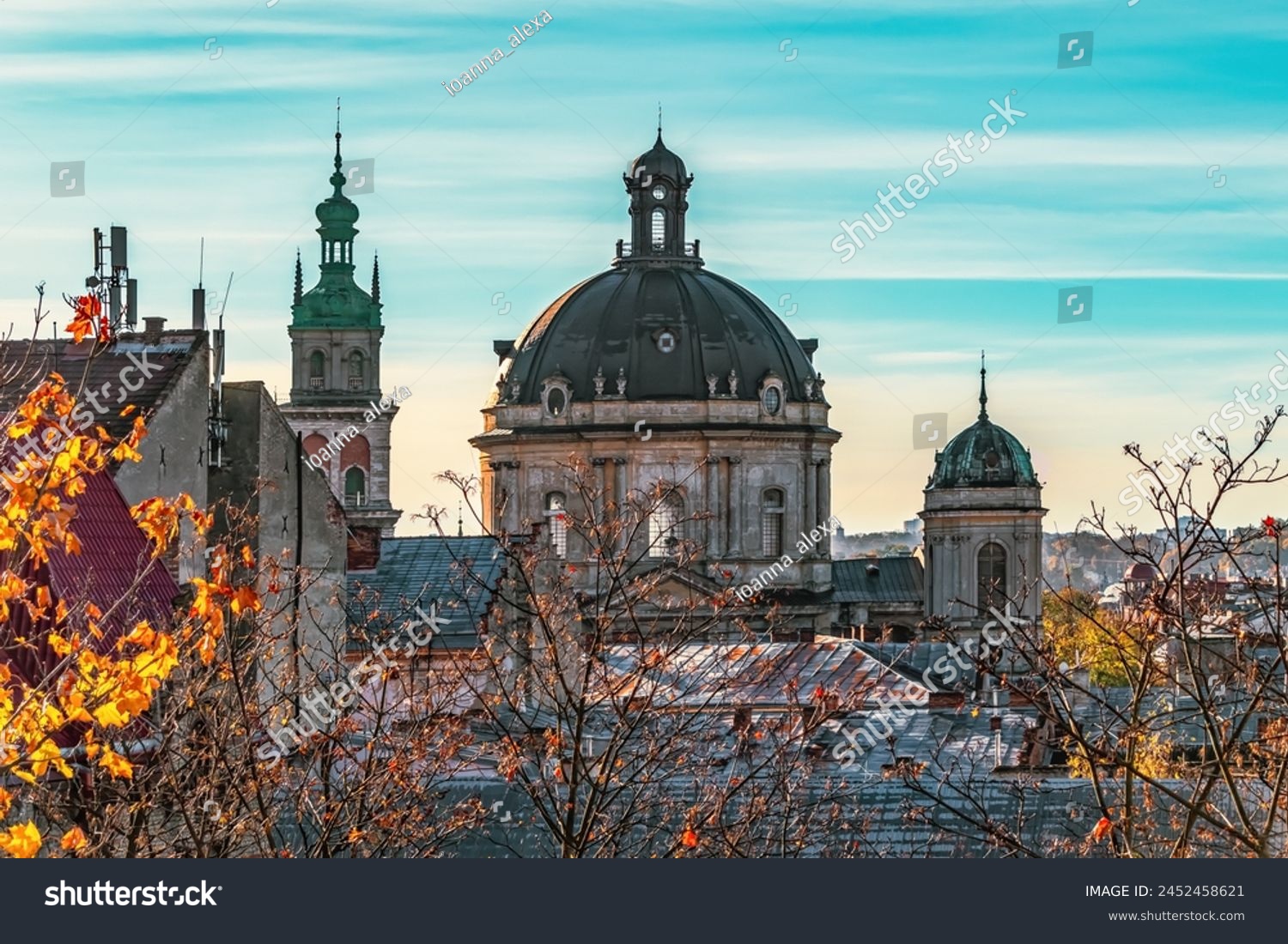 Dormition Church tower and Dominican Church dome in Lviv, Ukraine. Close-up of city roofs against the backdrop of bare tree branches on an autumn morning #2452458621