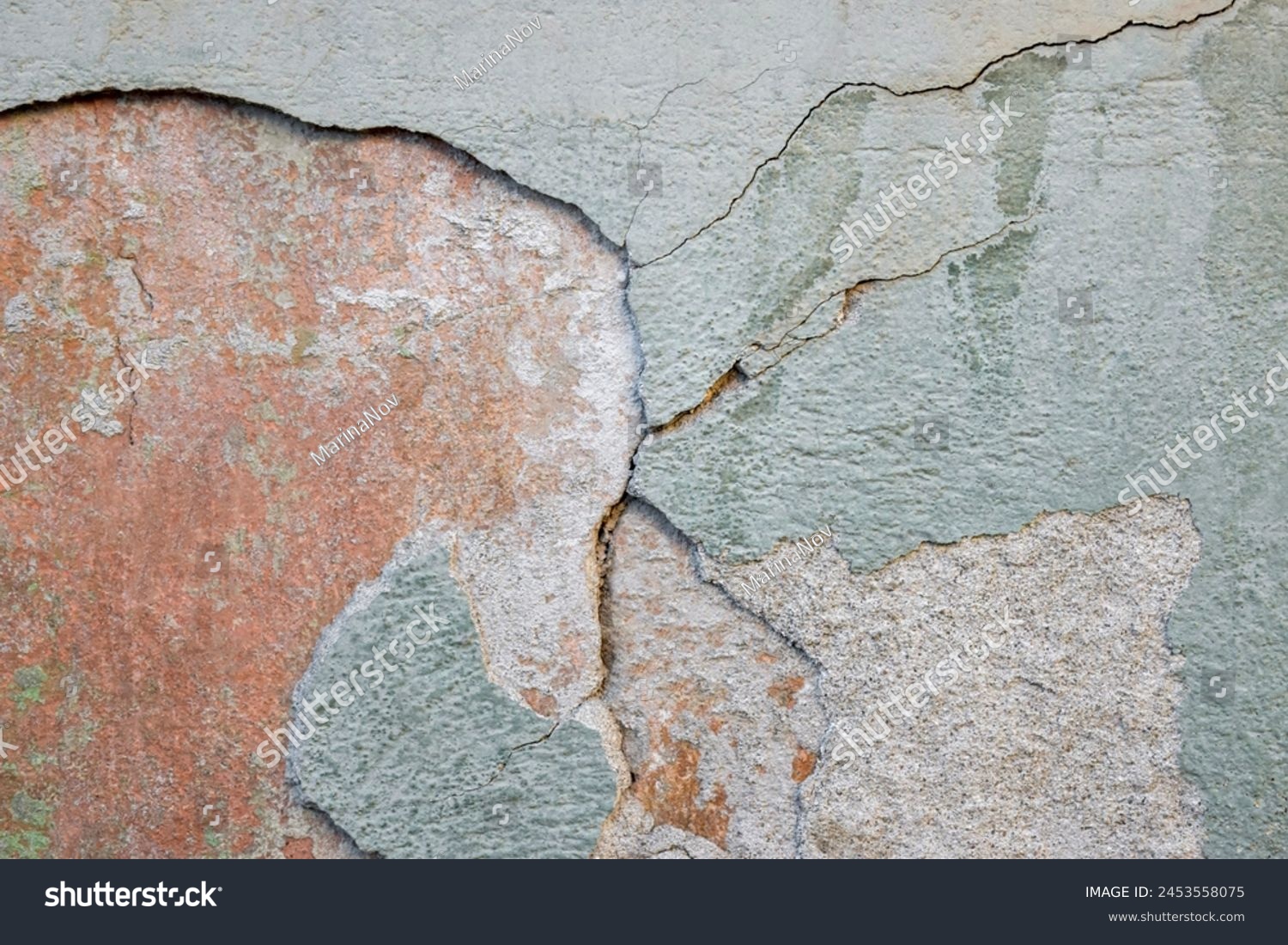 Colorful green-orange-yellow wall surface of an old building with crumbling plaster, cracks and stains as a textured background. Copy space. Selective focus. #2453558075
