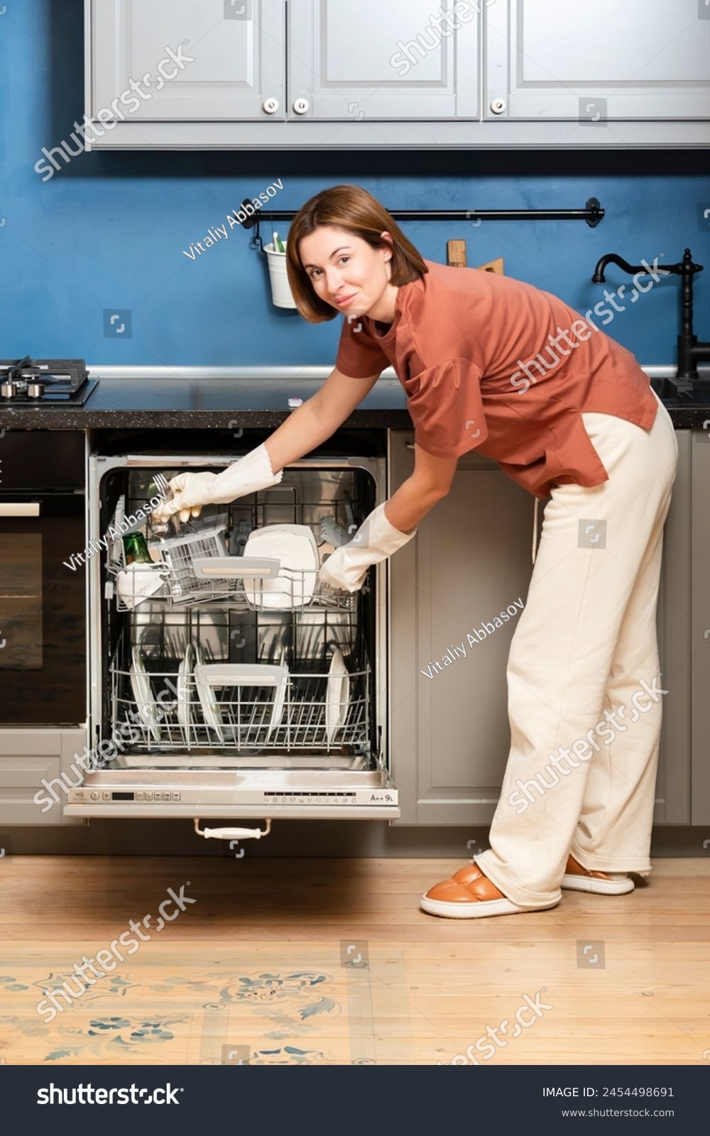 Busy housewife putting dirty plates in dishwasher machine in the kitchen. Household and exhausting cleaning day concept #2454498691