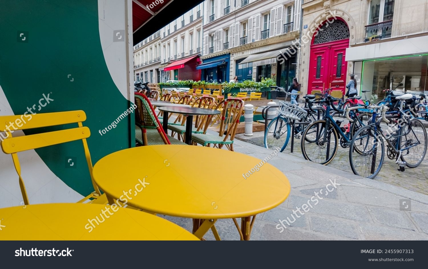 Colorful sidewalk cafe setting with yellow tables and chairs on a European city street, suggesting urban lifestyle and al fresco dining concepts #2455907313