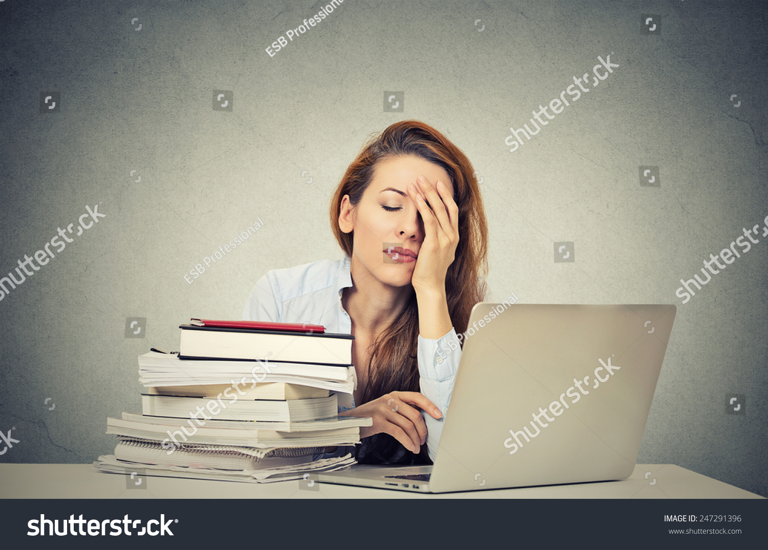 Too much work tired sleepy young woman sitting at her desk with books in front of laptop computer isolated grey wall office background. Busy schedule in college, workplace, sleep deprivation concept #247291396