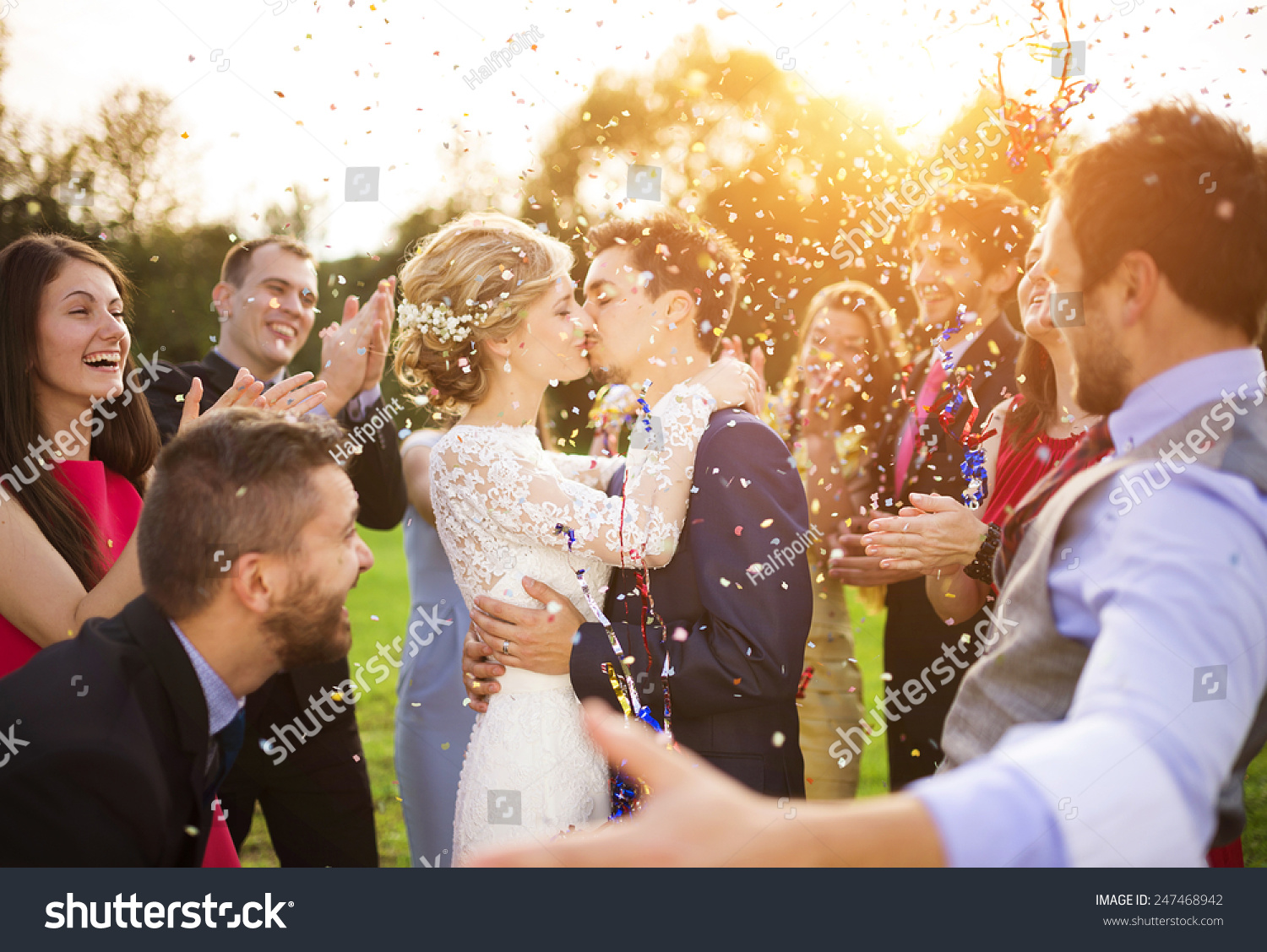 Full length portrait of newlywed couple and their friends at the wedding party showered with confetti in green sunny park #247468942