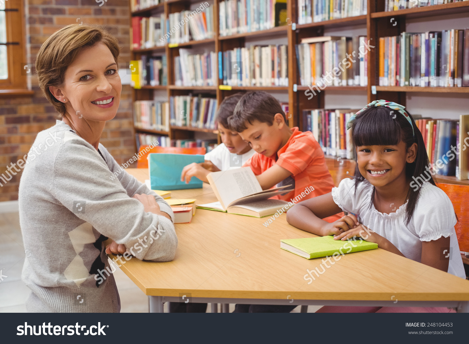 Cute pupils and teacher reading in library at the elementary school #248104453