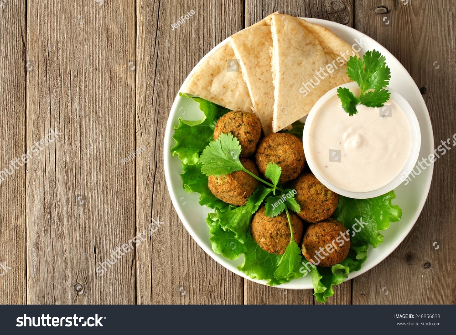 Plate of falafel with pita bread and tzatziki sauce on wooden table. View from above #248856838