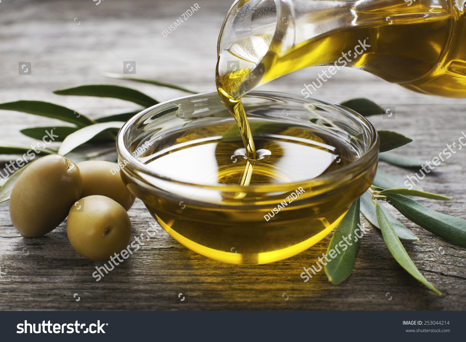 Bottle pouring virgin olive oil in a bowl close up #253044214