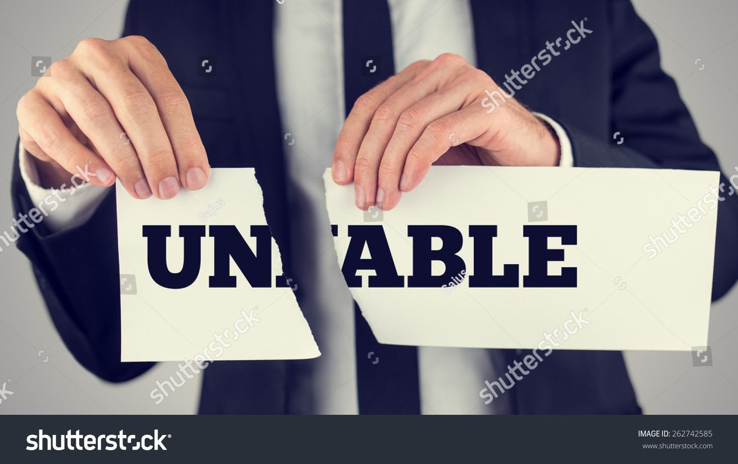 Retro vintage style image of a man holding a torn paper sign in his hands with the words - Un - Able- spread over the two halves depicting the concept of opposites. #262742585
