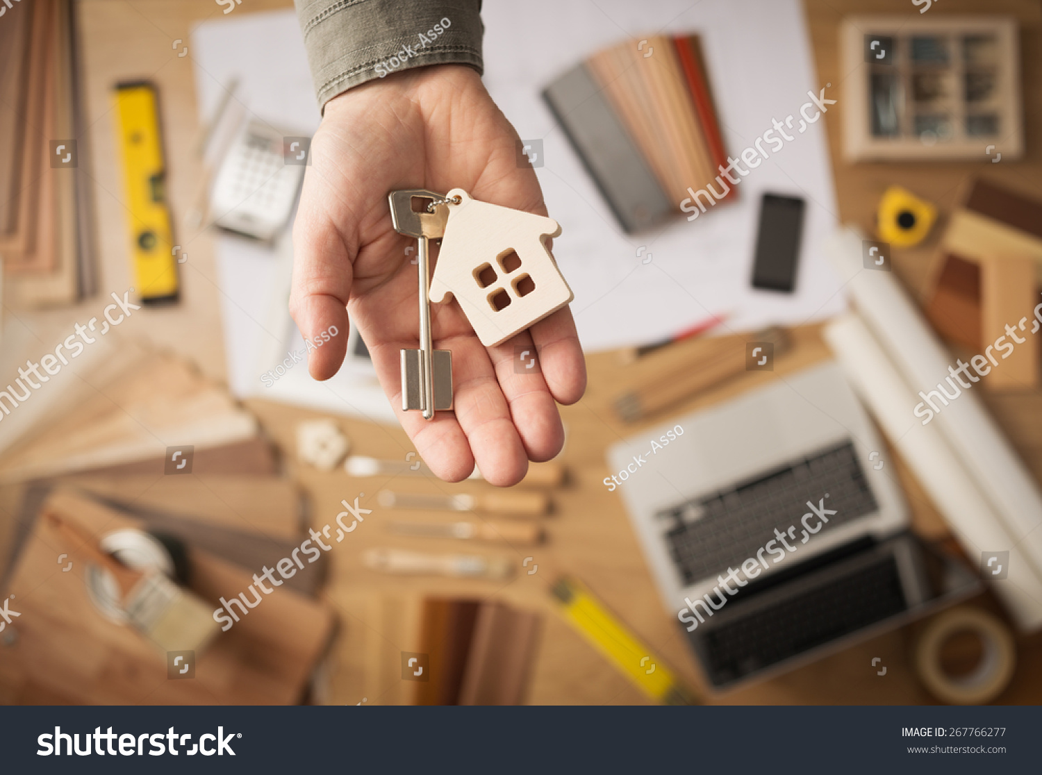 Real estate agent handing over a house key, desktop with tools, wood swatches and computer on background, top view #267766277