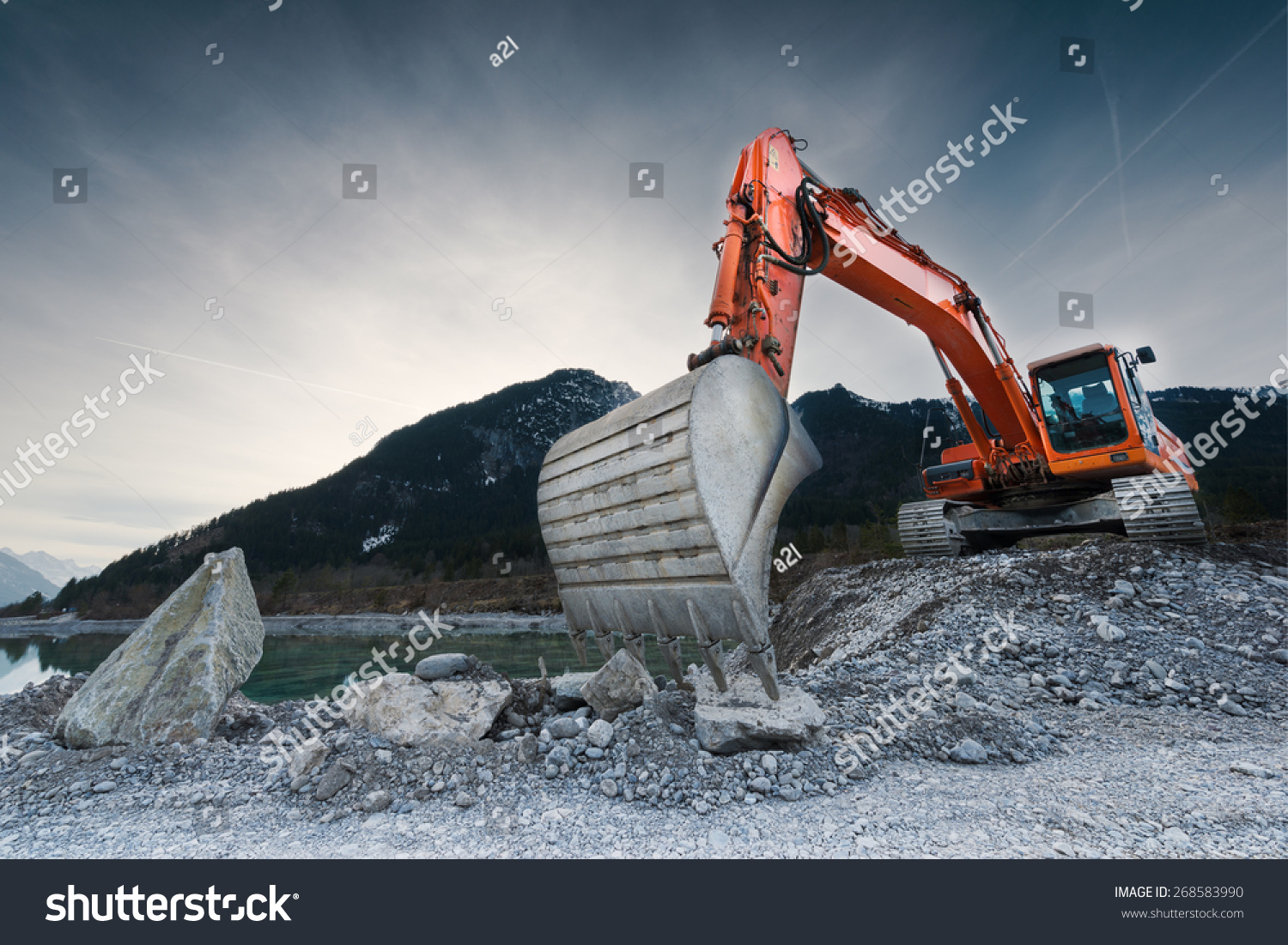 heavy organge excavator with shovel standing on hill with rocks #268583990