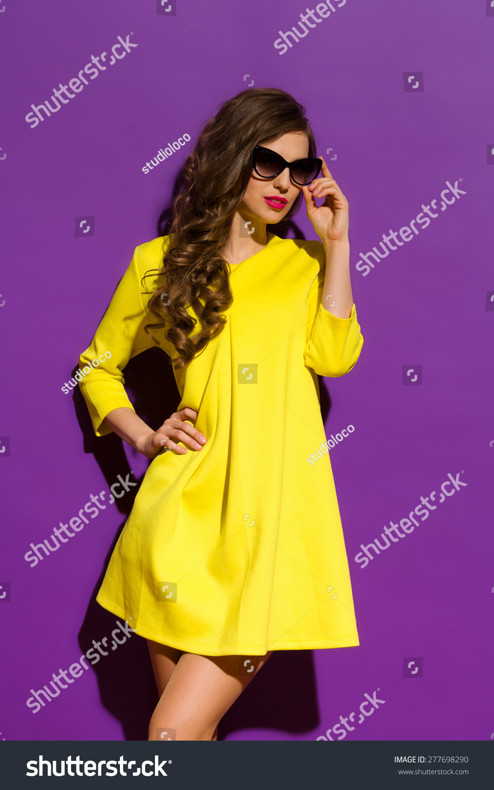 Fashion Model Posing On a Violet Background. Beautiful girl in sunglasses posing in yellow mini dress. Three quarter length studio shot on purple background. #277698290
