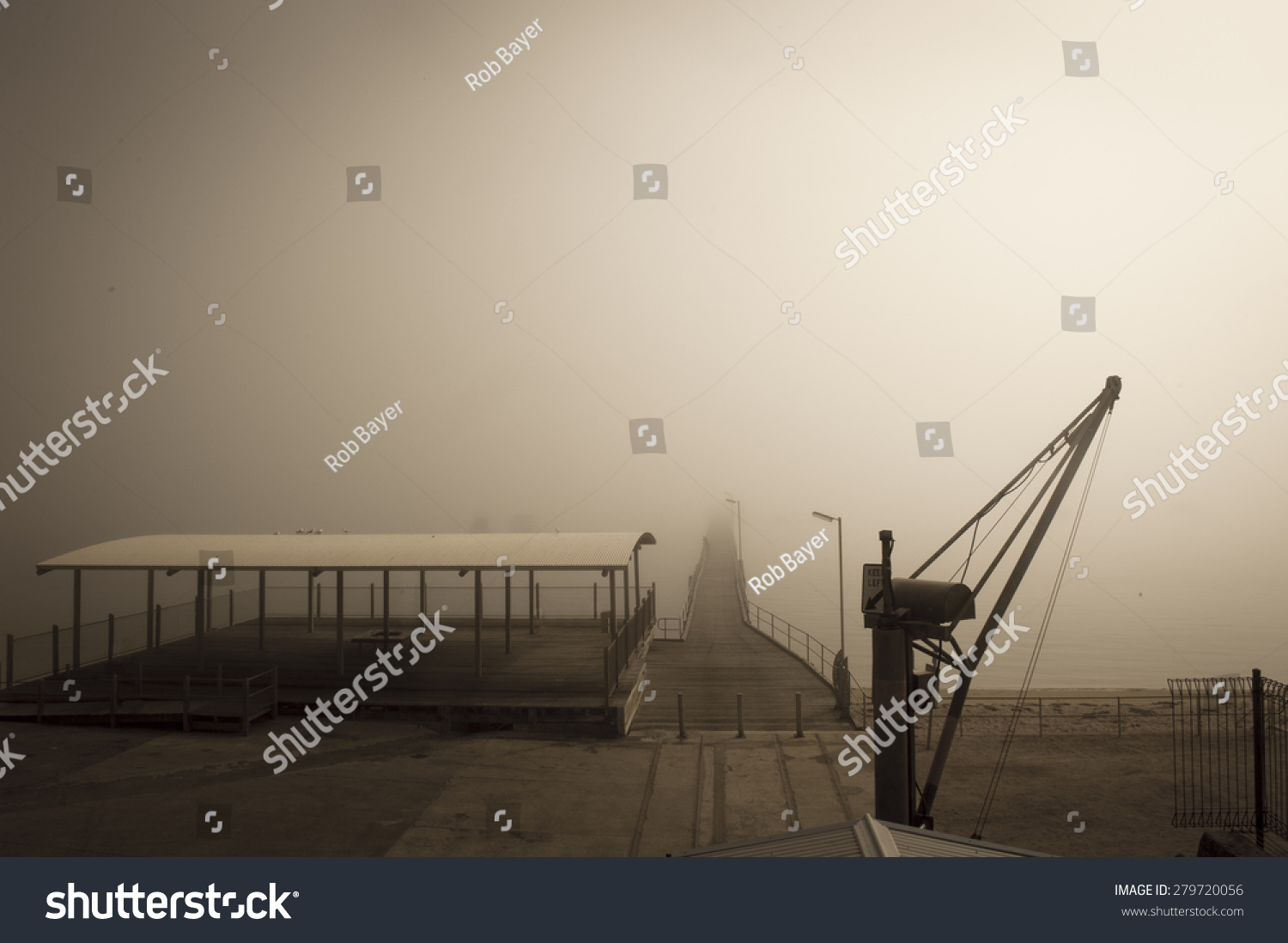 Filtered image of foggy harbour at ocean or lake or river water with crane and wooden jetty, blurred background and copy space. #279720056