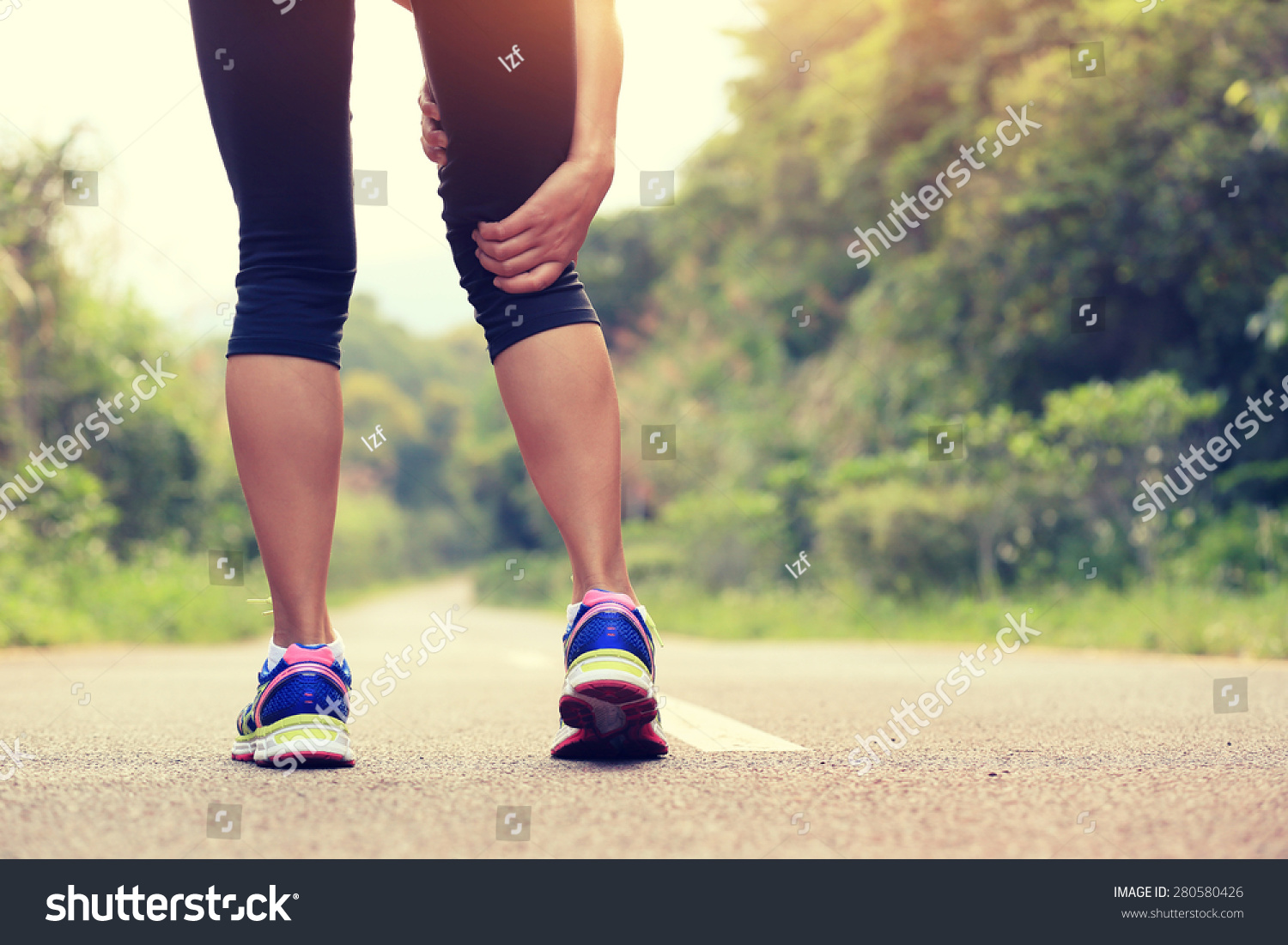 young fitness woman jogger hold her sports injured leg at forest trail  #280580426