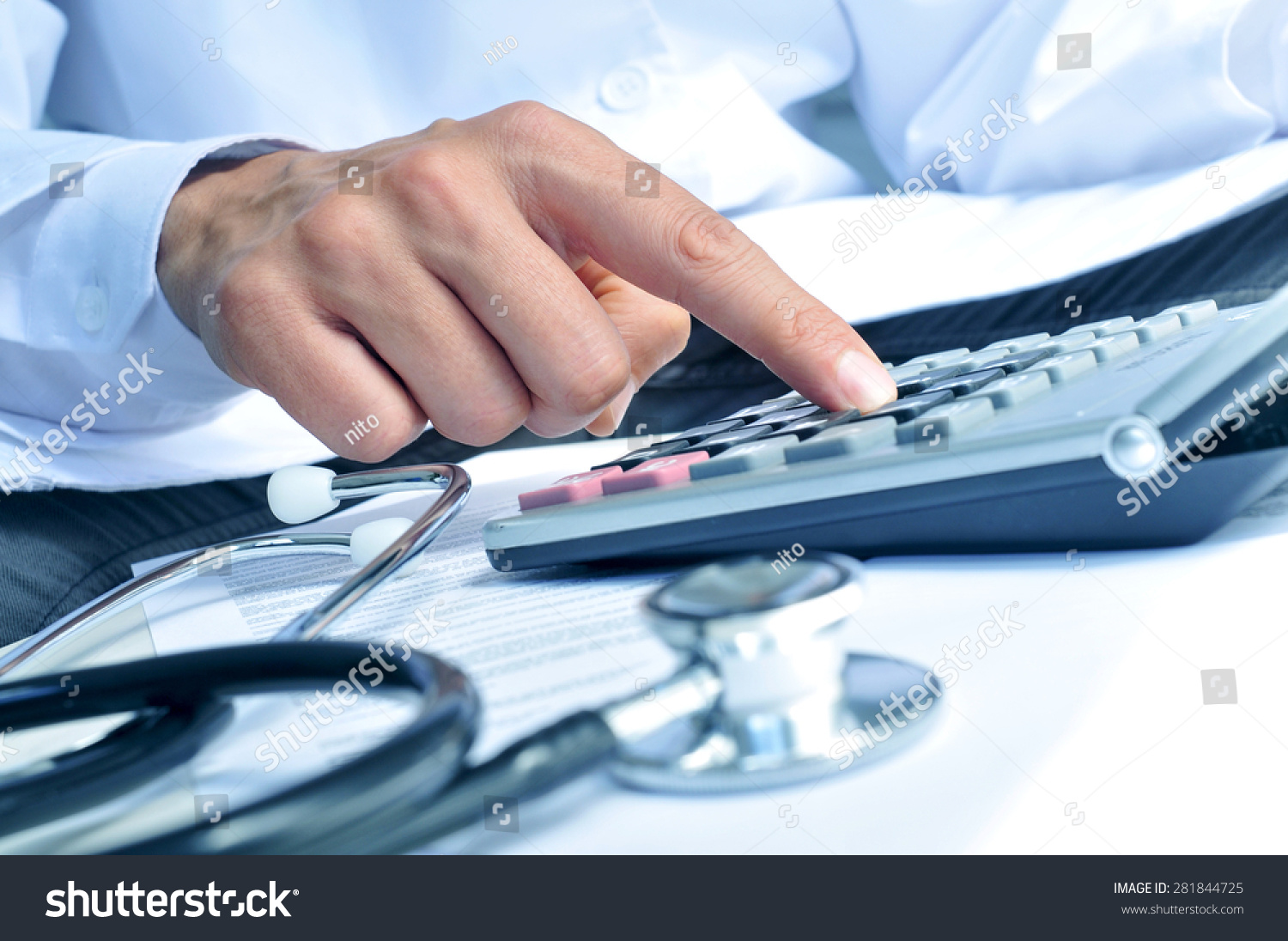 closeup of a young caucasian healthcare professional wearing a white coat calculates on an electronic calculator #281844725