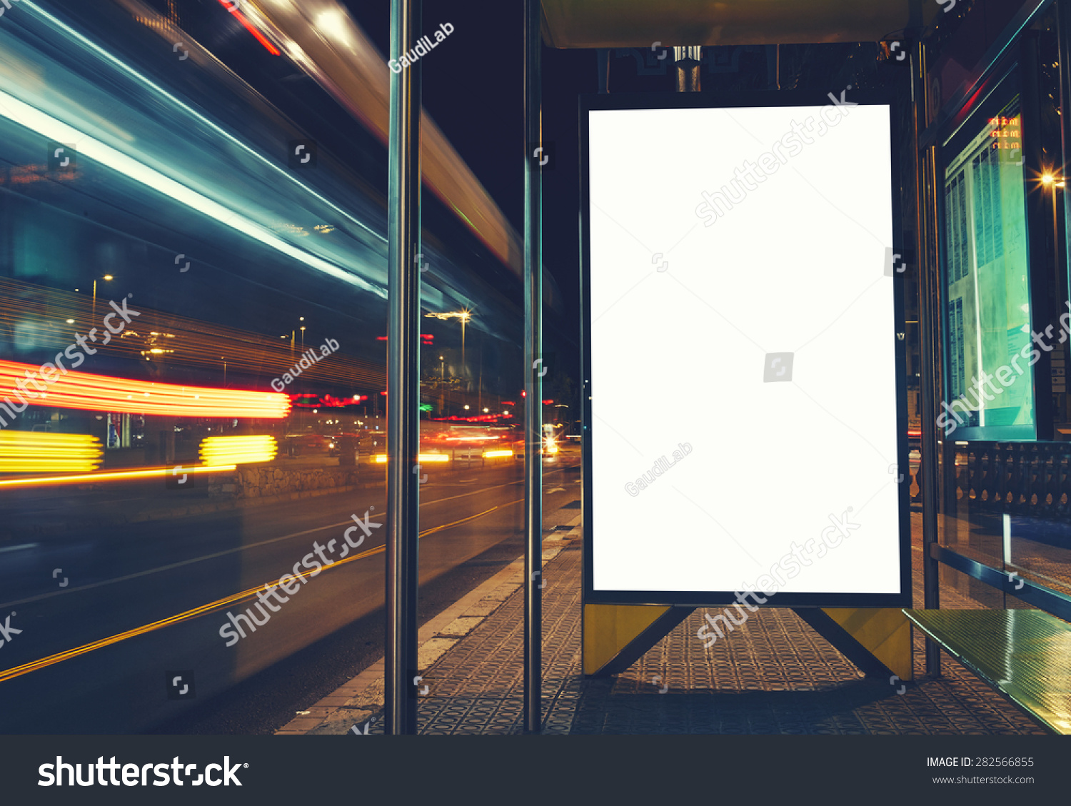 Illuminated blank billboard with copy space for your text message or content, advertising mock up banner of bus station, public information board with blurred vehicles in high speed in night city #282566855