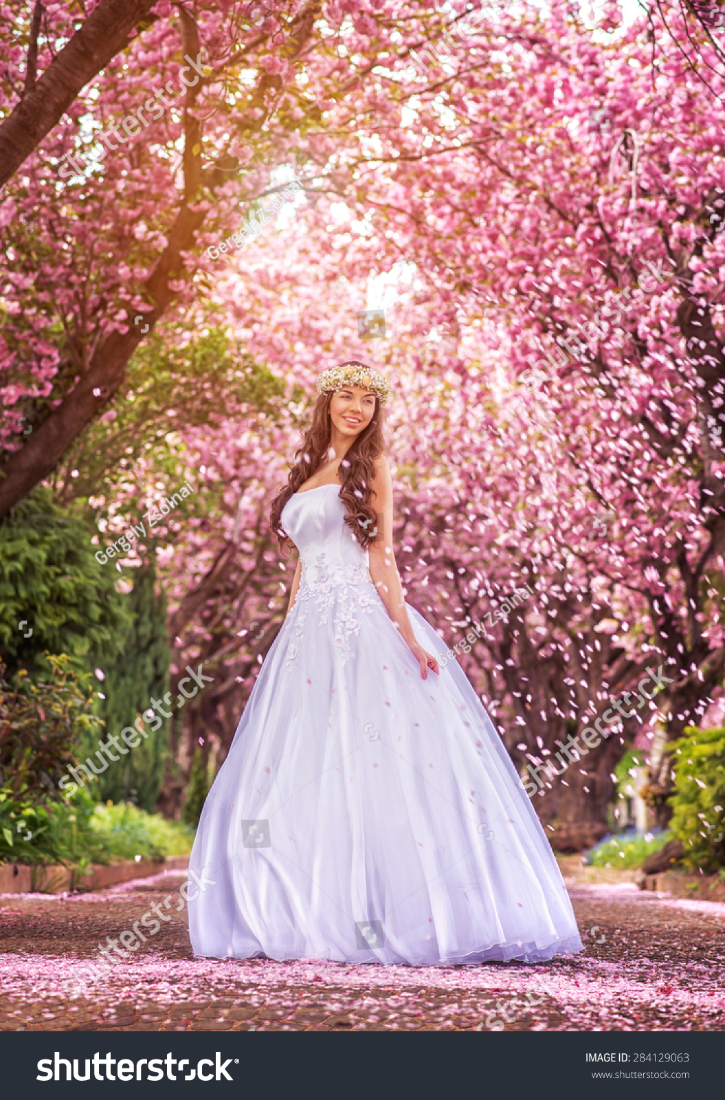 Beautiful bride in a white dress under the sakura tree and flower petals #284129063