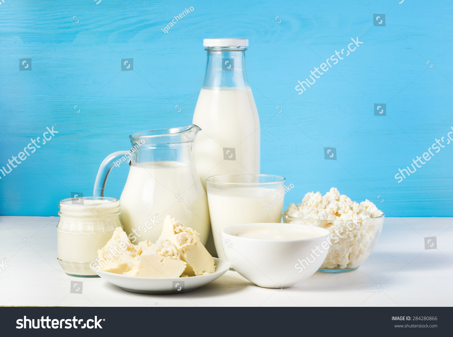 tasty healthy dairy products on a table on a blue background: sour cream in a white bowl, cottage cheese in bowl, cream in a a bank,  butter on a saucer and milk in a jar, glass bottle and in a glass #284280866