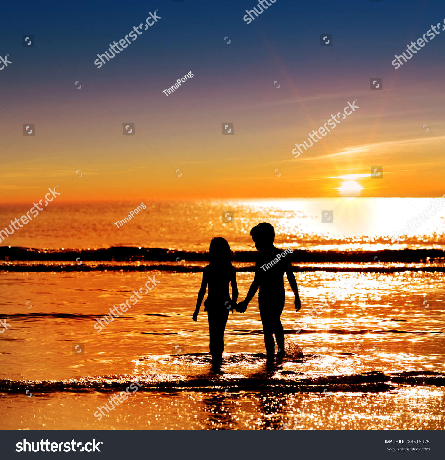Silhouette boy holding  girl hand on the sea against the strong sunrise #284516975
