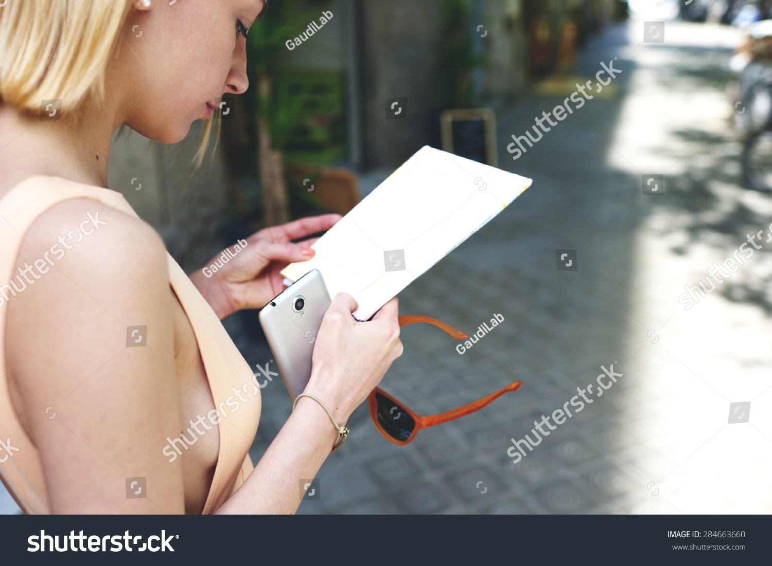 Cropped image caucasian female tourist holding blank copy space paper and smart phone in the hands while she strolling in the city,young gorgeous woman read empty flyer while standing in urban setting #284663660