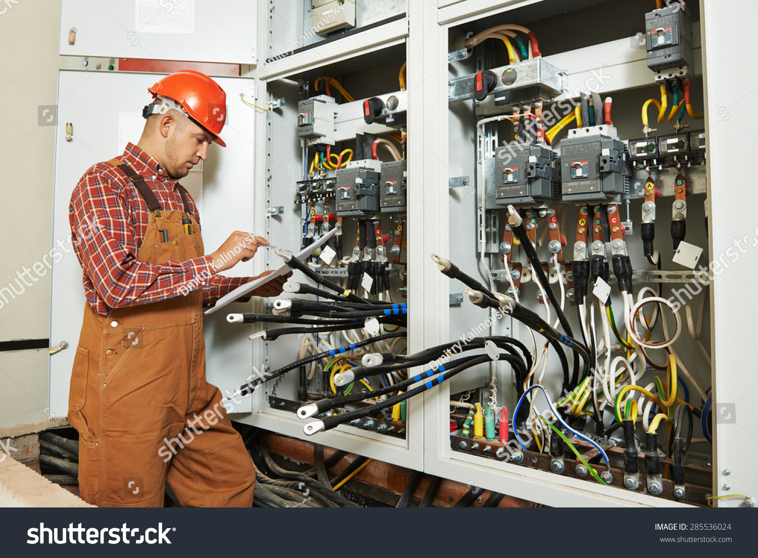 adult electrician builder engineer worker with electric scheme plan in front of fuse switch board #285536024