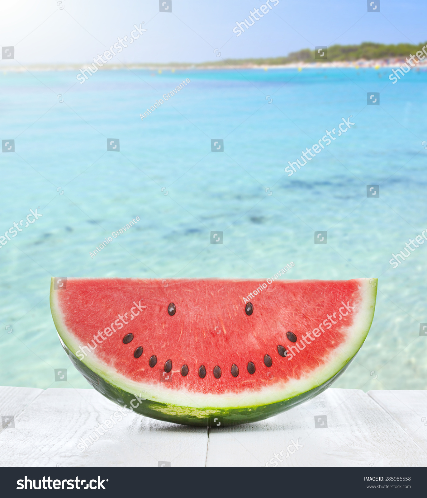 Slice of watermelon with seeds that make a smiling face on the beach #285986558