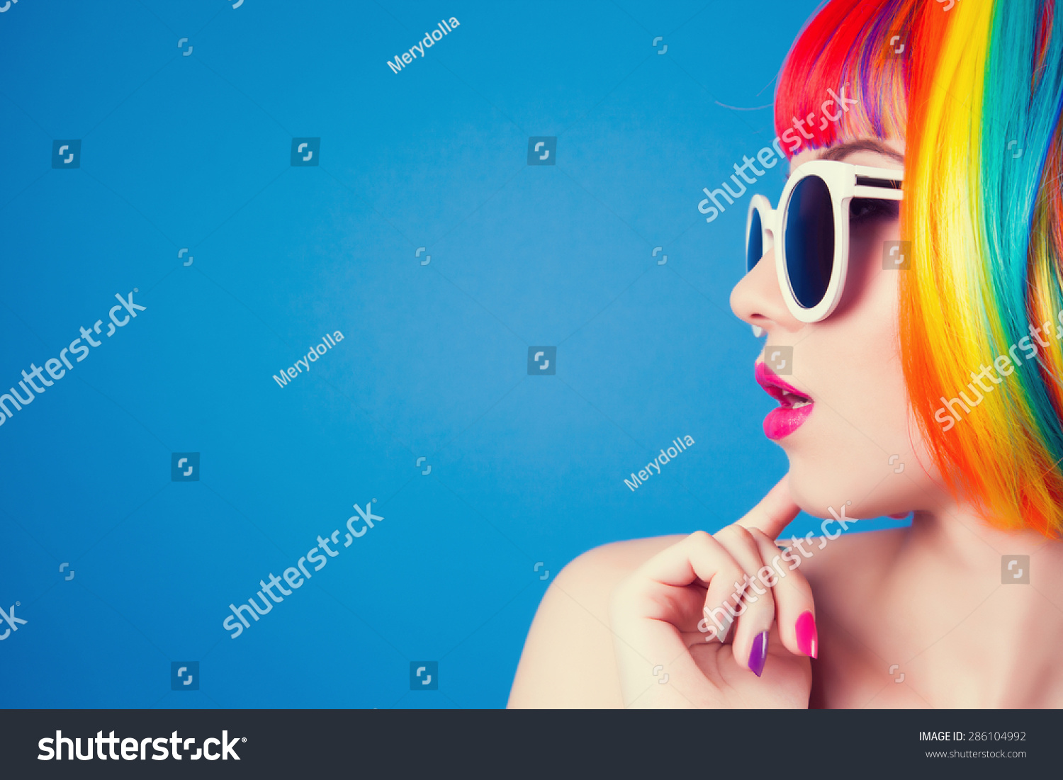 beautiful woman wearing colorful wig and white sunglasses against blue background #286104992