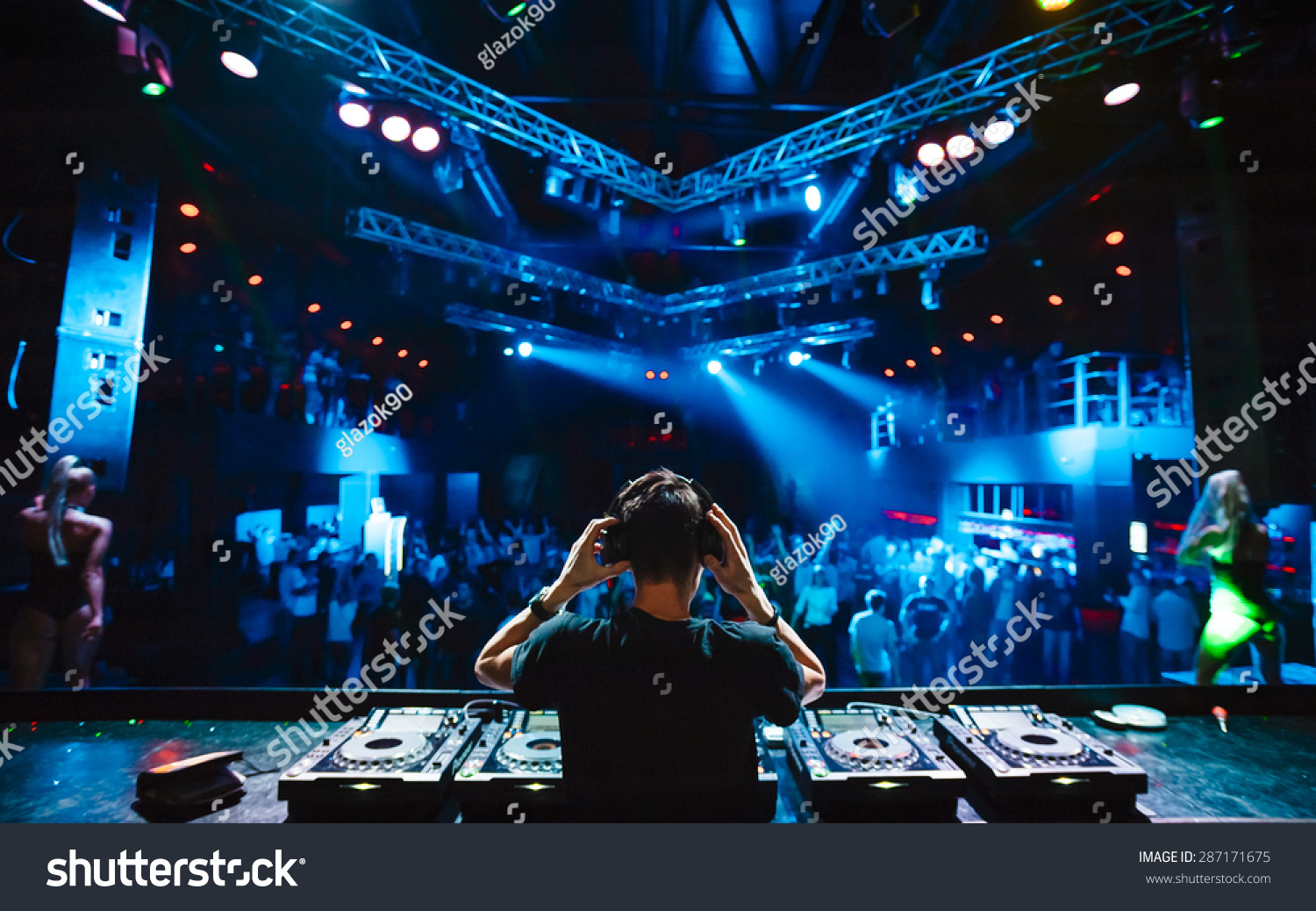 DJ with headphones at night club party under the blue light and people crowd in background #287171675