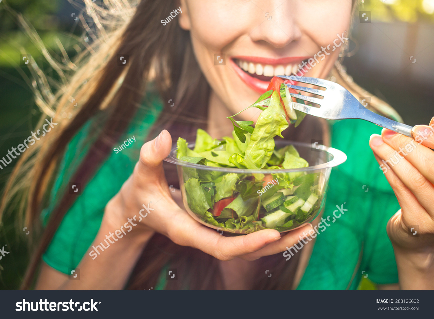 Portrait of attractive caucasian smiling woman eating salad, focus on hand and fork. soft, backlight #288126602