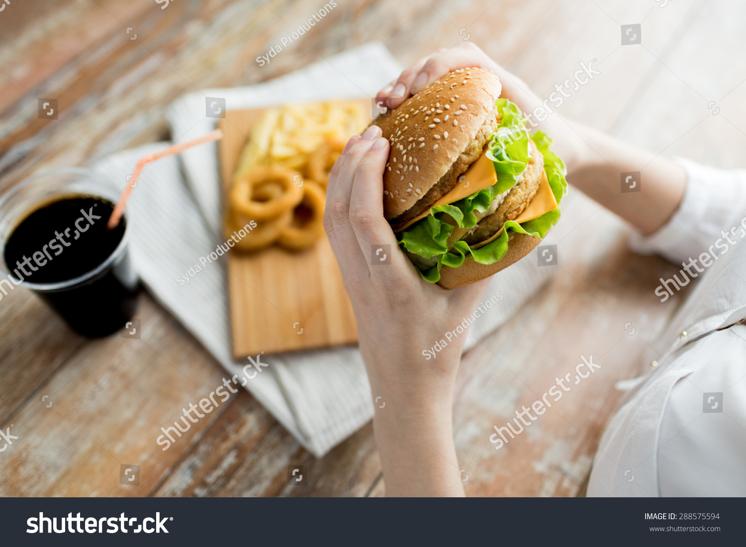 fast food, people and unhealthy eating concept - close up of woman hands holding hamburger or cheeseburger #288575594