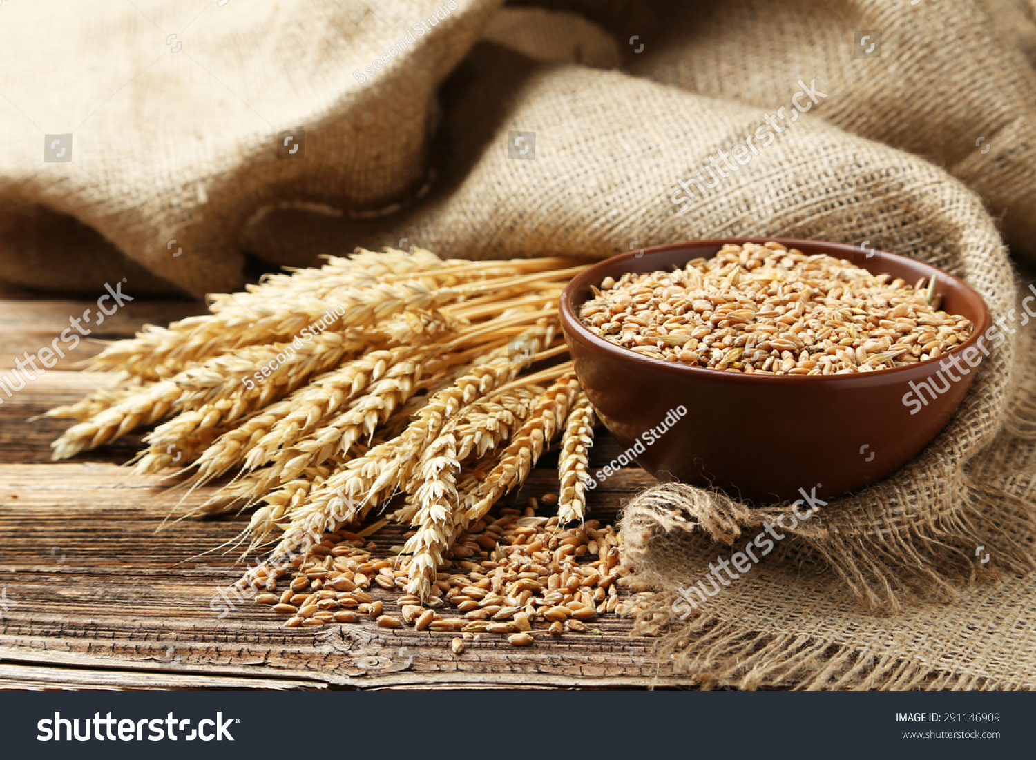 Ears of wheat and bowl of wheat grains on brown wooden background #291146909