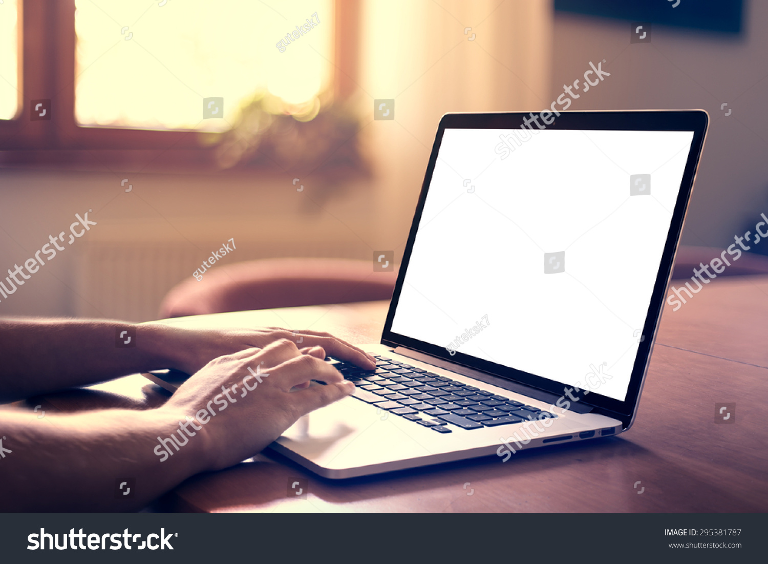 Man's hands using laptop with blank screen on desk in home interior. #295381787