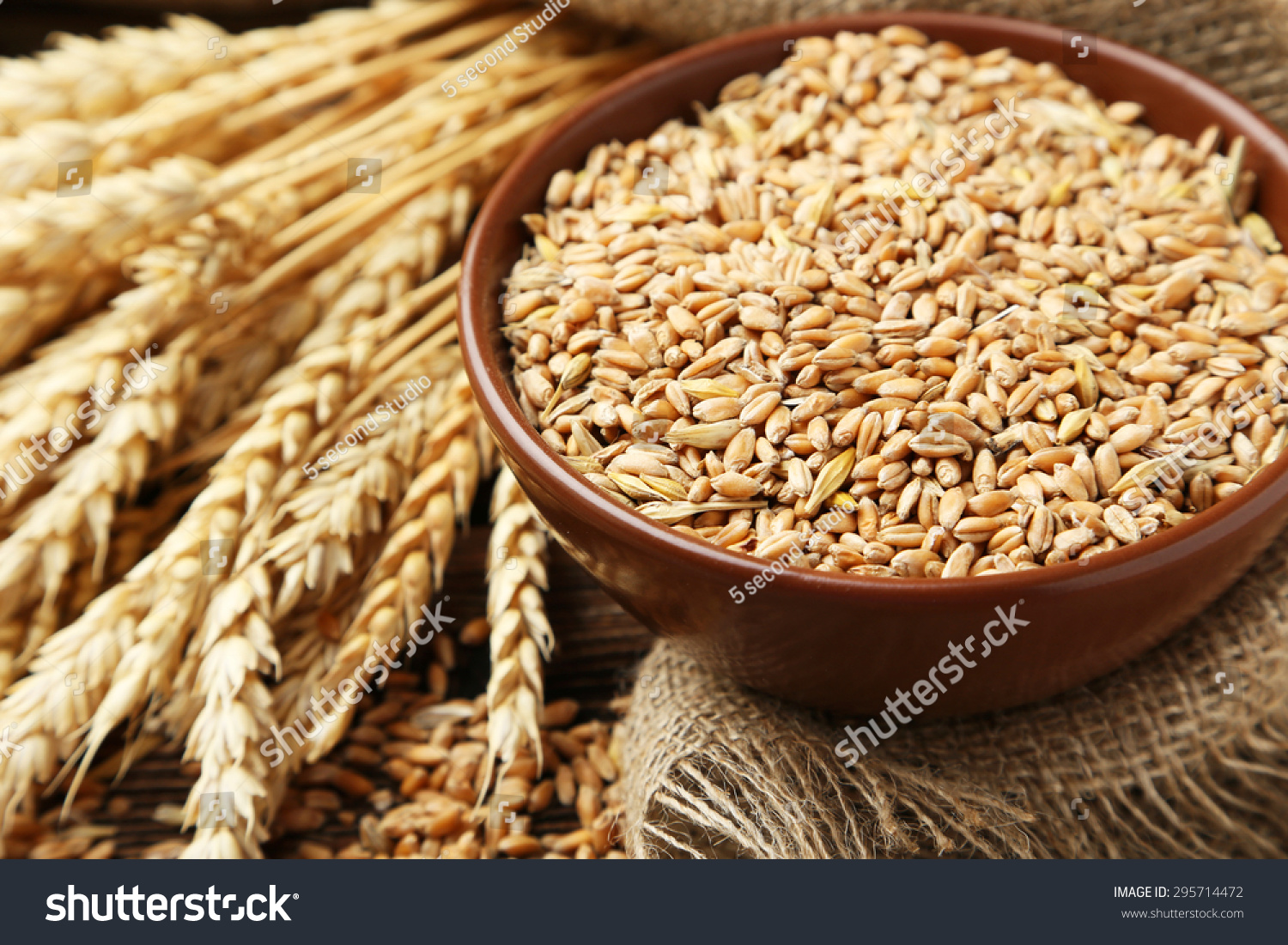 Ears of wheat and bowl of wheat grains on brown wooden background #295714472