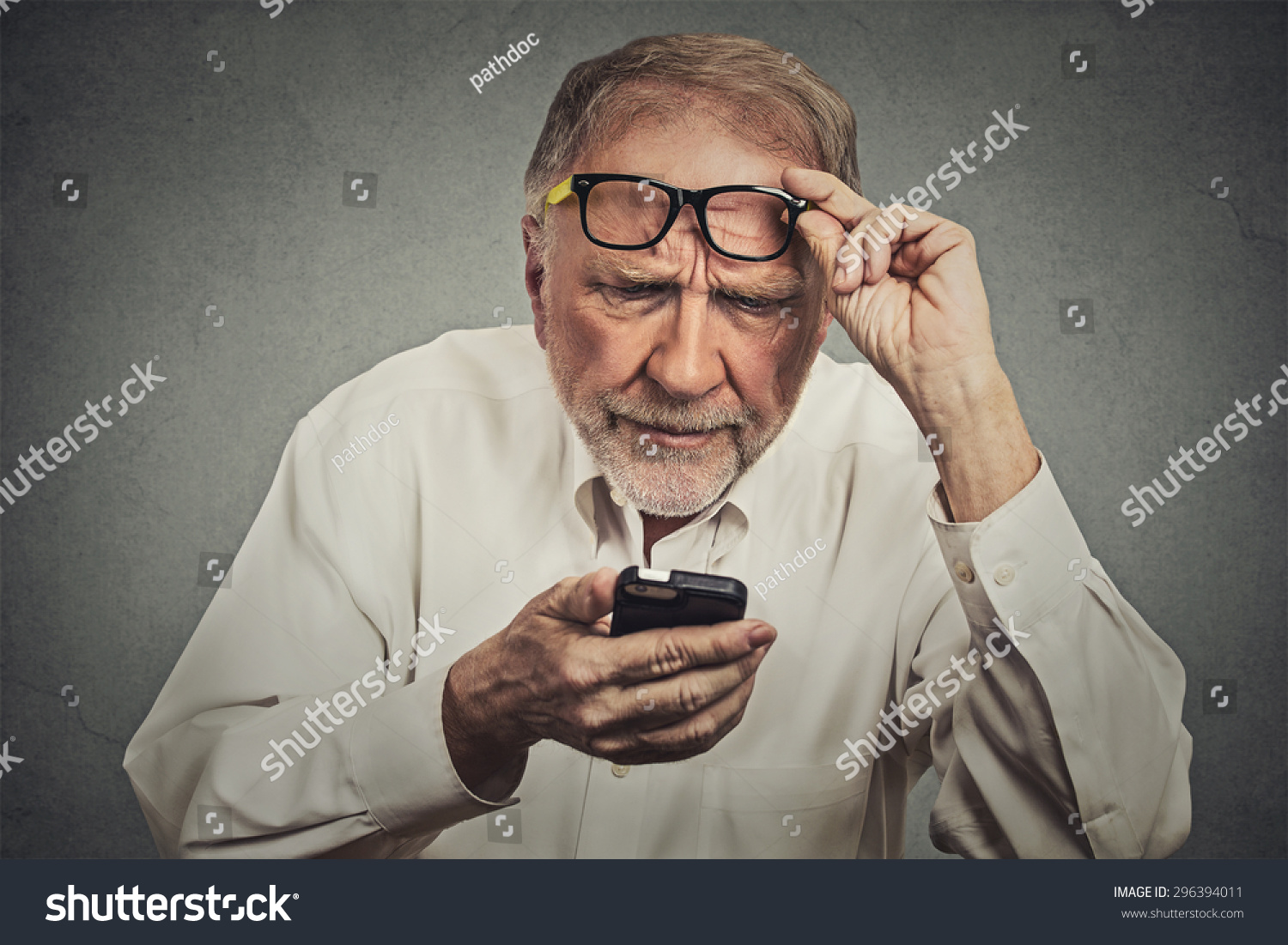 Closeup portrait headshot elderly man with glasses having trouble seeing cell phone has vision problems. Bad text message. Negative human emotion facial expression perception. Confusing technology #296394011
