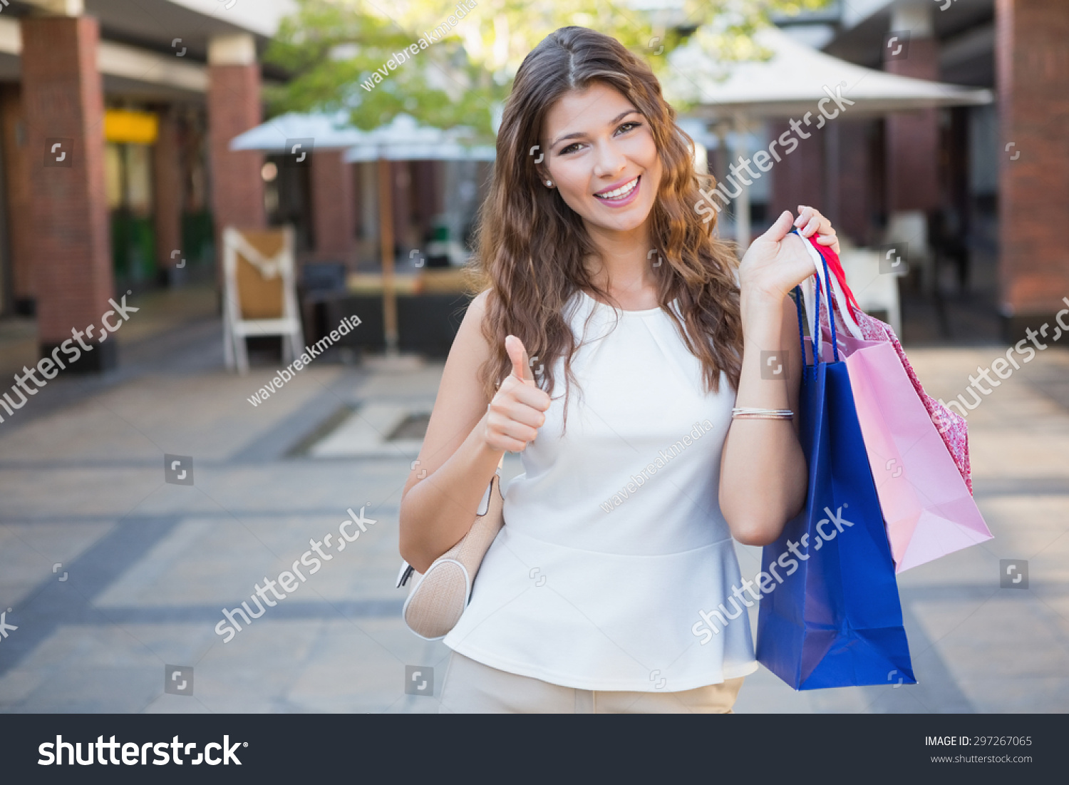 Portrait of smiling woman with shopping bags looking at camera and showing thumbs up at the shopping mall #297267065