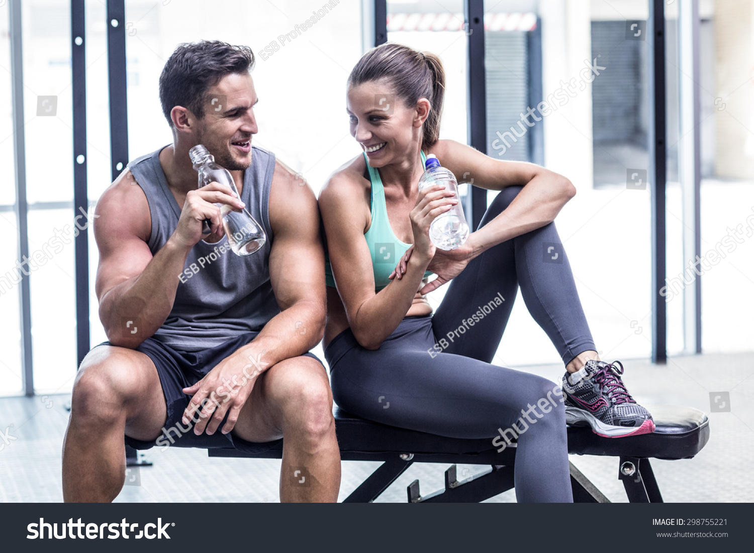 Muscular couple discussing on the bench and holding water bottle #298755221
