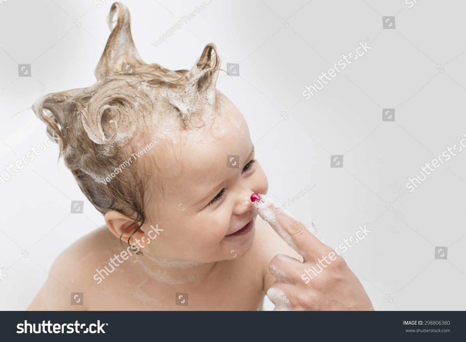 Little pretty wet baby boy in bath room with foam soap hair sitting and playing with mother's hand on white background, horizontal picture #298806380