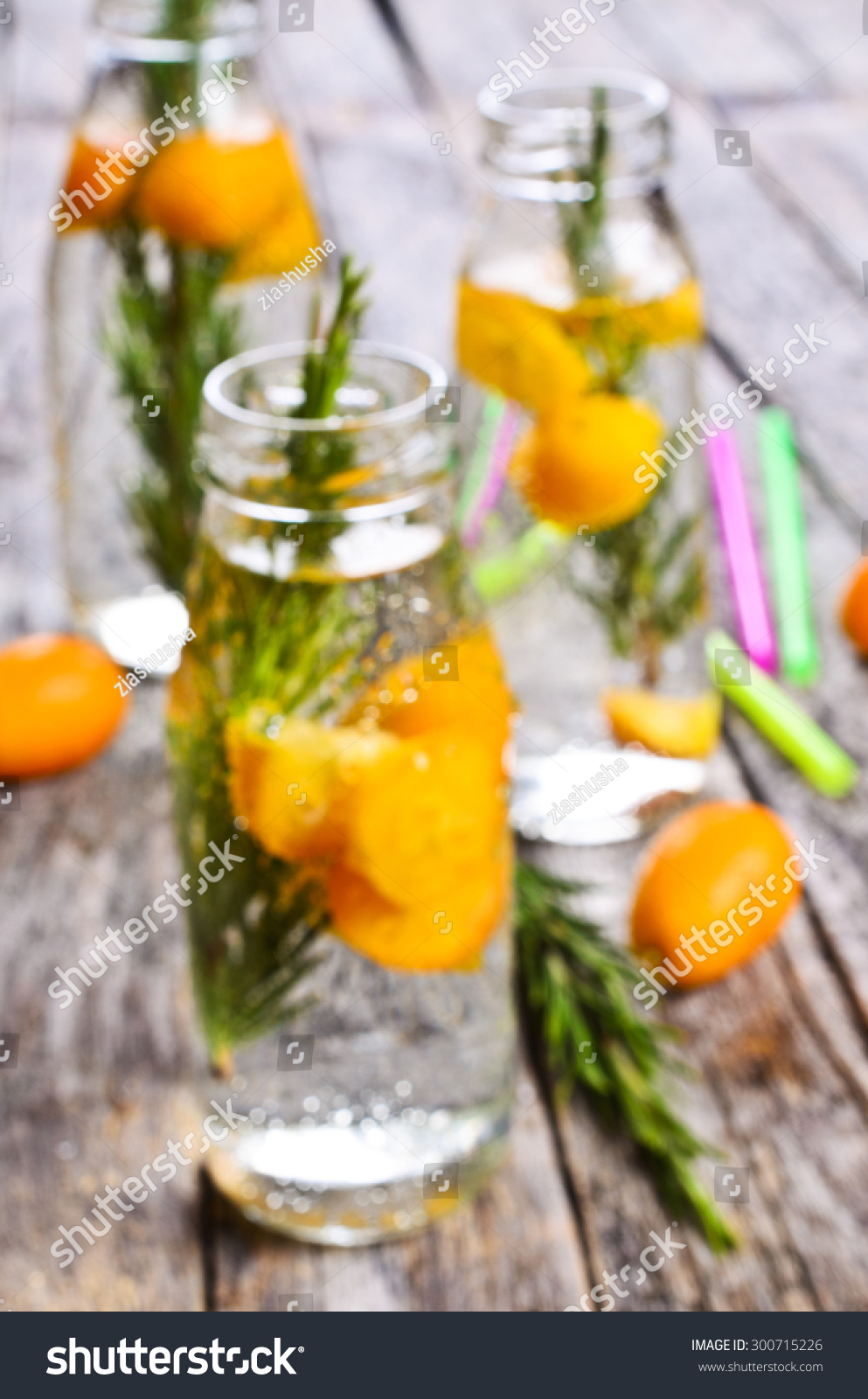 Blurred background: bottles with a clear liquid, citrus and rosemary on a wooden surface #300715226