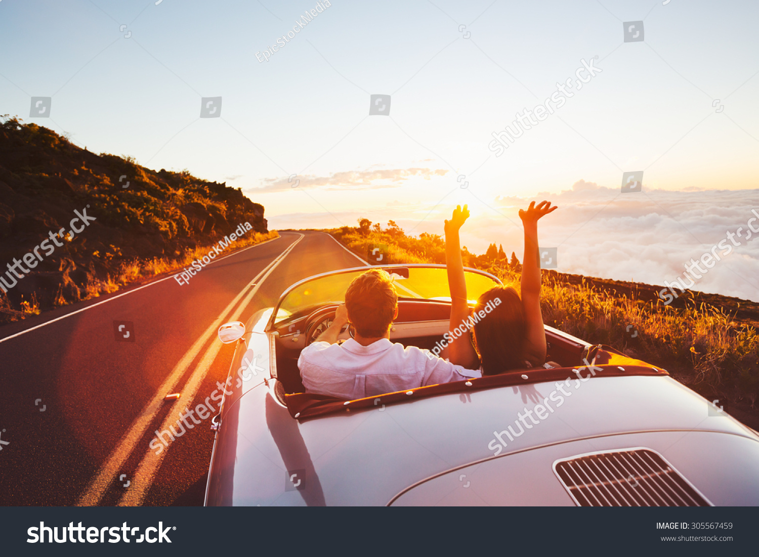 Happy Couple Driving on Country Road into the Sunset in Classic Vintage Sports Car  #305567459