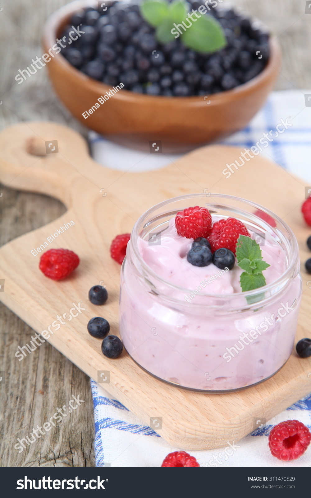 Yogurt and ripe blueberries and raspberries on a wooden table. Summer dessert. #311470529