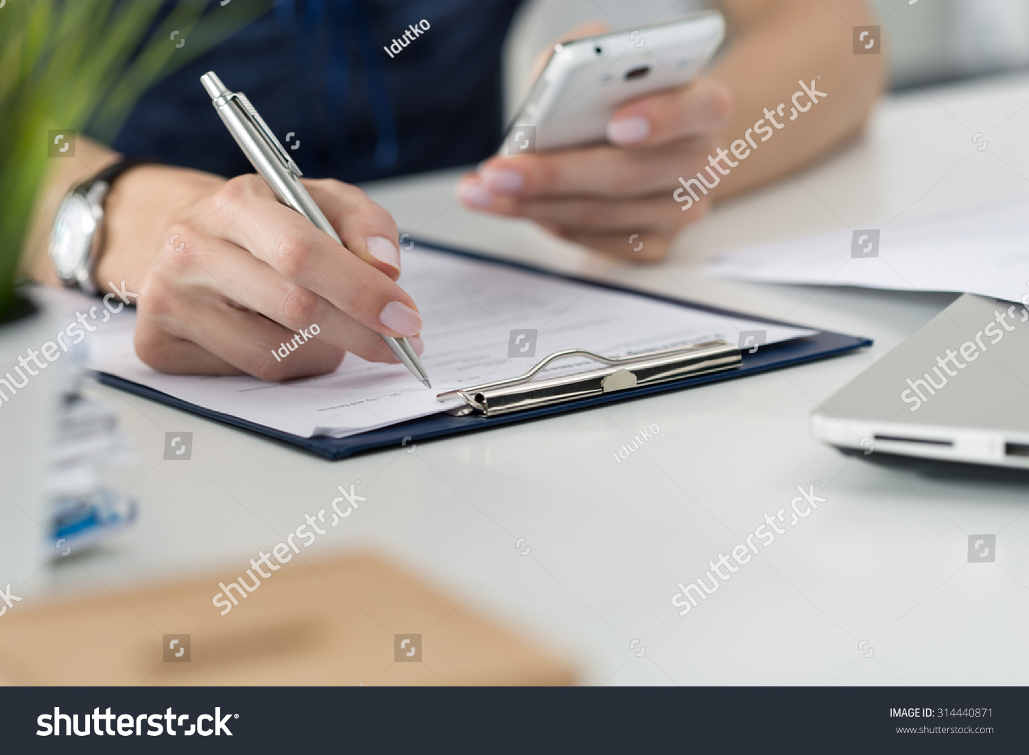 Close-up of female hands. Woman writting something and looking at mobile phone screen sitting at her office #314440871