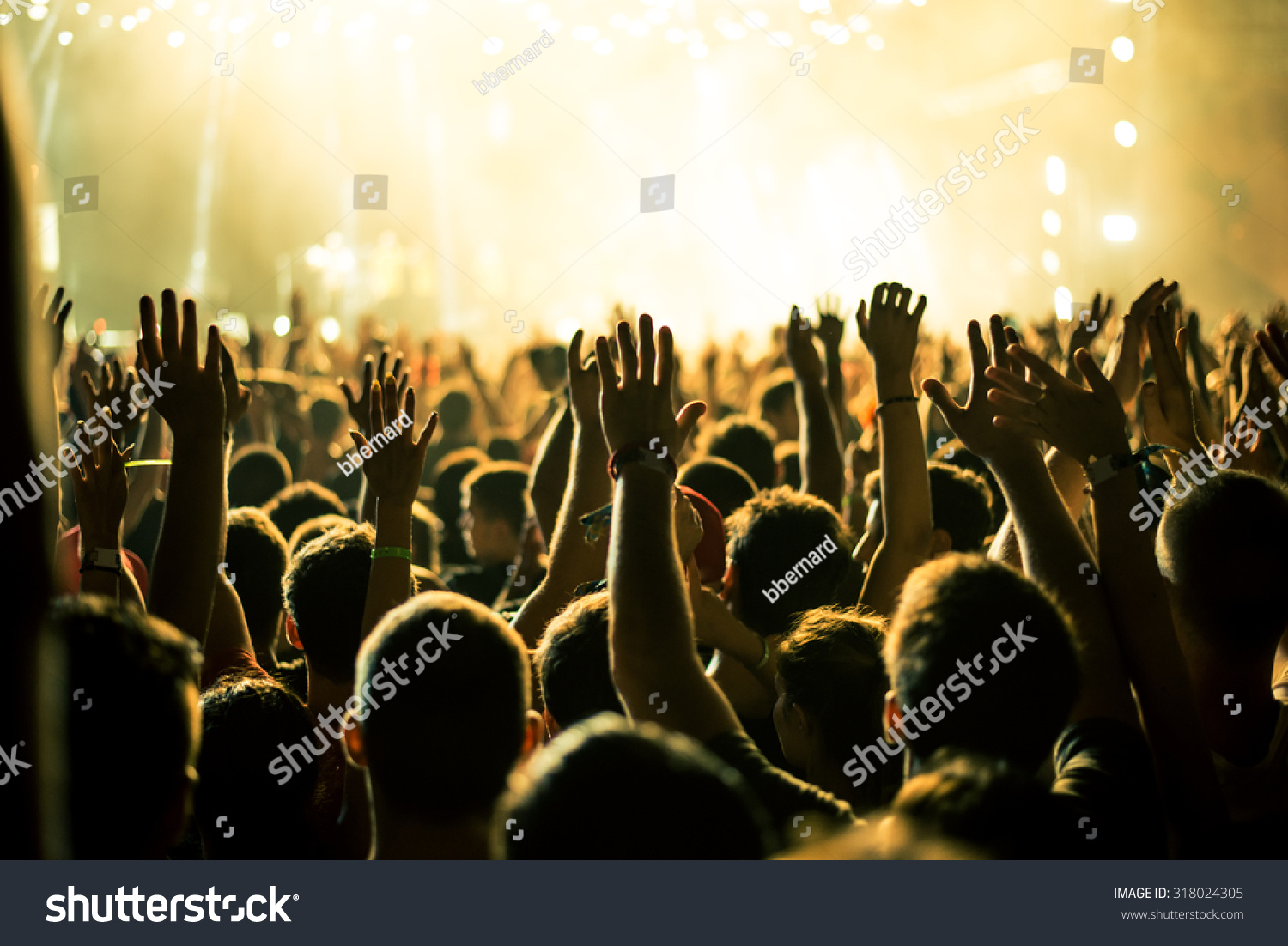 Audience with hands raised at a music festival and lights streaming down from above the stage. Soft focus, blurred movement. #318024305