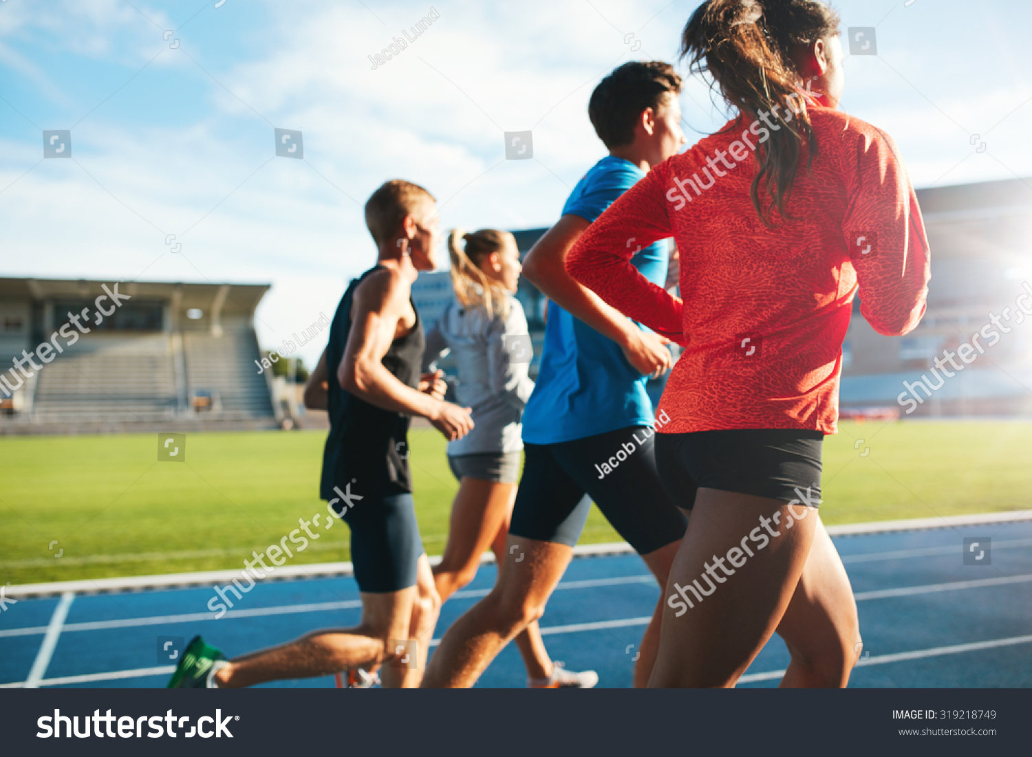 Rear view of young people running together on race track. Young athletes practicing a run on athletics stadium track. #319218749