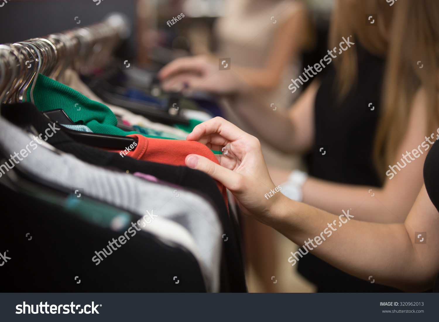 Young beautiful women shopping in fashion mall, choosing new clothes, looking through hangers with different casual colorful garments on hangers, close up of hands #320962013