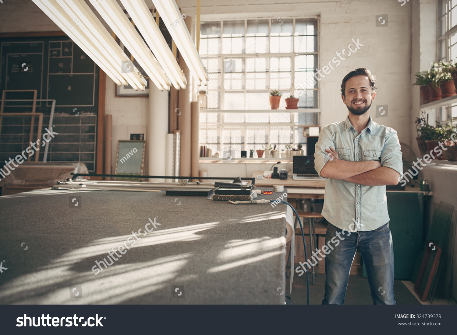 Portrait of a good looking male designer standing in his workshop studio with his arms folded and smiling confidently at the camera #324739379