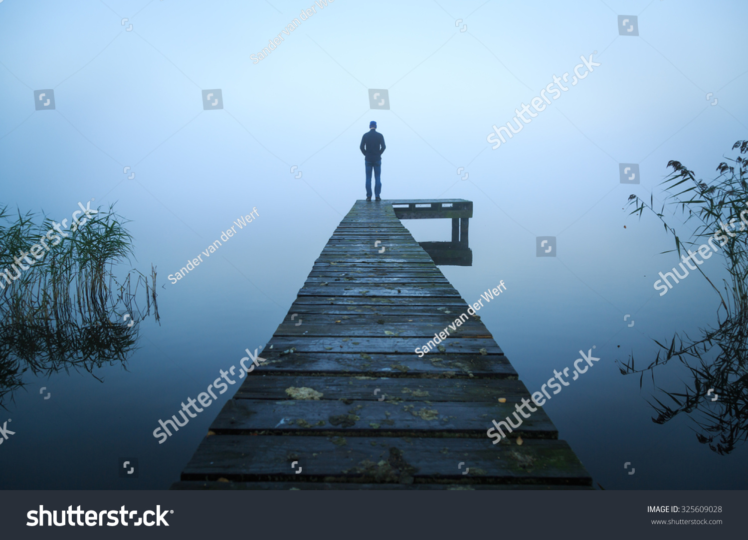 Depressed emotions concept: man standing at the end of a jetty, on a foggy, autumn morning. #325609028