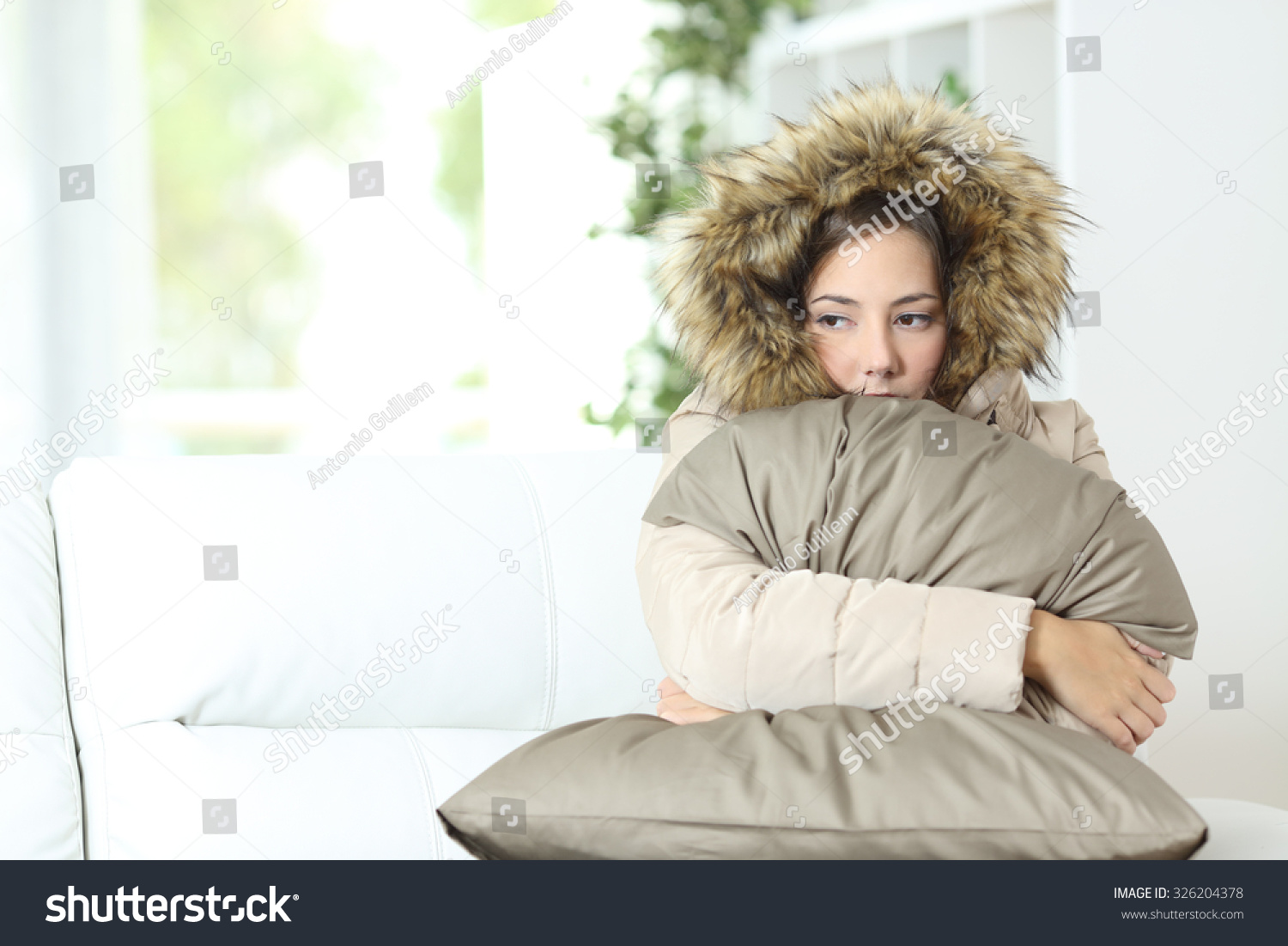 Angry woman warmly clothed in a cold home sitting on a couch #326204378