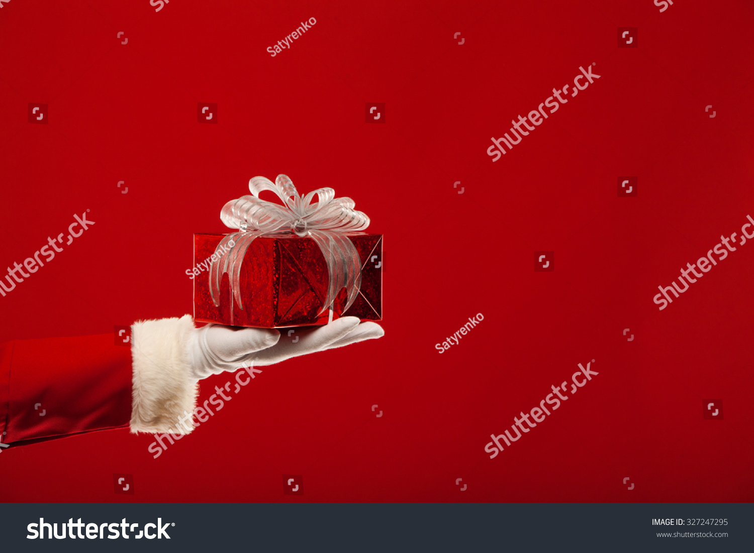 Christmas. Photo of Santa Claus gloved hand with red gift box, on a red background #327247295