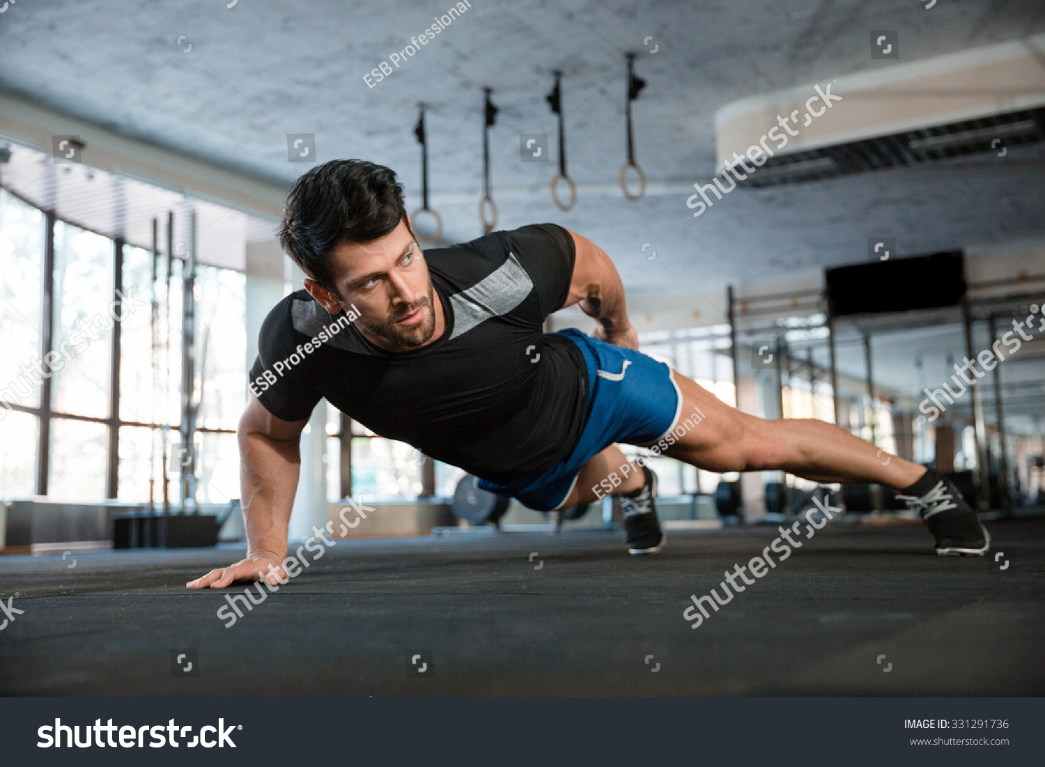 Portrait of a handsome man doing push ups exercise with one hand in fitness gym #331291736