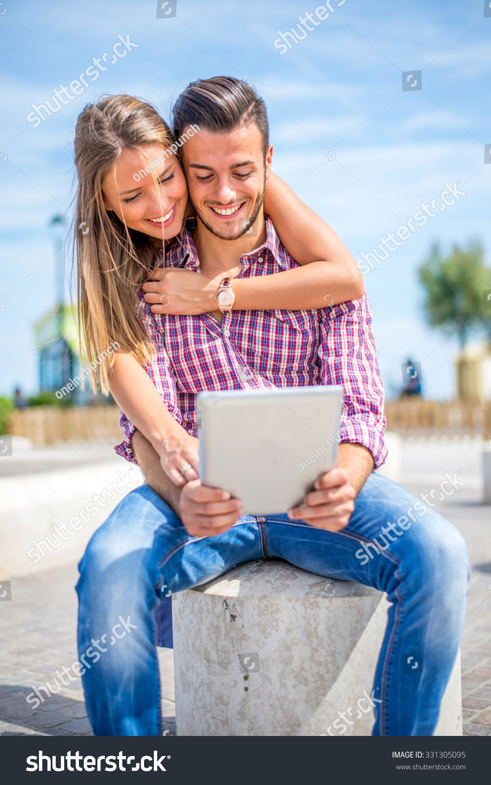 Beautiful couple sitting on a bench outdoors and looking at tablet - Lovers having fun with new technology and shopping online #331305095