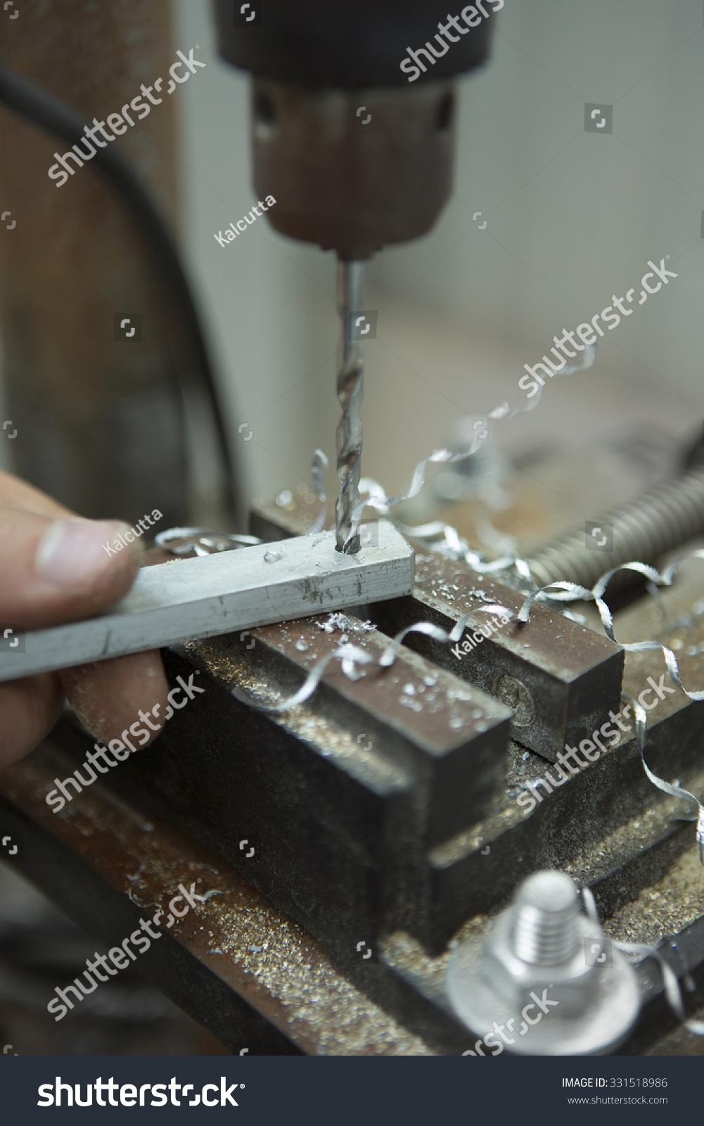 Man drilling in Steel Plate with Bench Drill. Close-up Electric drilling machine with manual pressure, a man holding a metal part and the hole is drilled, pressing drill to the workpiece surface #331518986